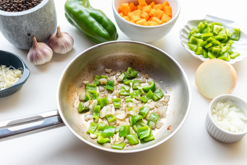 A vibrant image of green bell peppers and onions being sautéed, surrounded by fresh vegetables and spices.